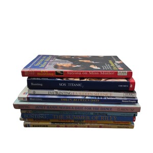 May include: A stack of children's books with titles including "Spying on Miss Müller", "SOS Titanic", and "The Summer of Riley". The books have colorful covers and are stacked on top of each other.