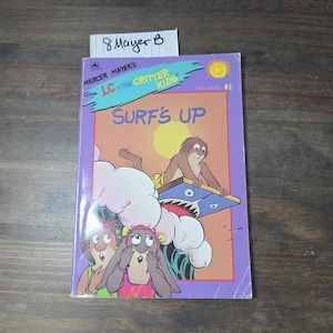 May include: A children's book titled "LC + The Critter Kids Surf's Up" by Mercer Mayer. The cover features cartoon characters surfing, with a purple border and a yellow sun. The book is a mini novel, number 1.
