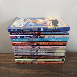 May include: A stack of 12 paperback books featuring the cover art of the popular children's series "Sabrina the Teenage Witch". The books are arranged vertically with the titles visible. The titles include "Up, Up, and Away", "Know-It-All", "Age of Aquariums", "Pirate Pandemonium", "Showdown at the Mall", "All That Glitters", "Prisoner of Cabin 13", "Sabrina Goes to Rome", "A Dog's Life", and "Ben There, Done That".