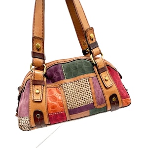 May include: A patchwork handbag with a variety of colors including red, orange, purple, green, and tan. The bag has a brown leather handle and trim, with gold-colored hardware. The bag features a mix of textures and patterns.