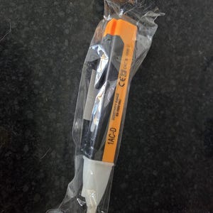 May include: A black and orange 1AC-D voltage tester in a clear plastic package. The tester has a white tip and an orange top. Text on the tester reads "Sensitivity Range 50-1000VAC" and "CAT III 1000 V".