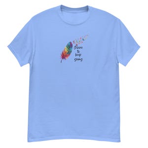 May include: A light blue short-sleeve t-shirt featuring a graphic of a multicolored feather that transitions into small flying birds. The text "Choose to keep going" is printed in black script lettering next to the feather design.