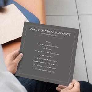Peut inclure: Une personne tient une carte grise avec le texte "FULL STOP EMERGENCY RESET" et les mots "RESET STATE" au-dessus. Les instructions de la carte incluent "Stop", "Asseyez-vous" et "Expirez lentement."