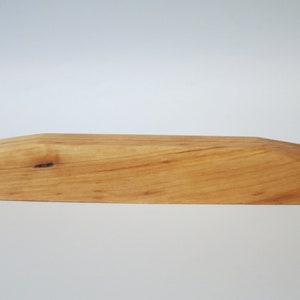 Op de afbeelding: Een natuurlijke houten displaystandaard met een licht gebogen bovenkant en een knoop in het hout.
