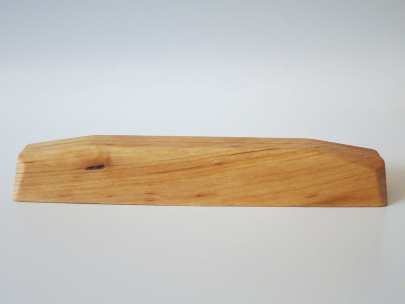 Op de afbeelding: Een natuurlijke houten displaystandaard met een licht gebogen bovenkant en een knoop in het hout.