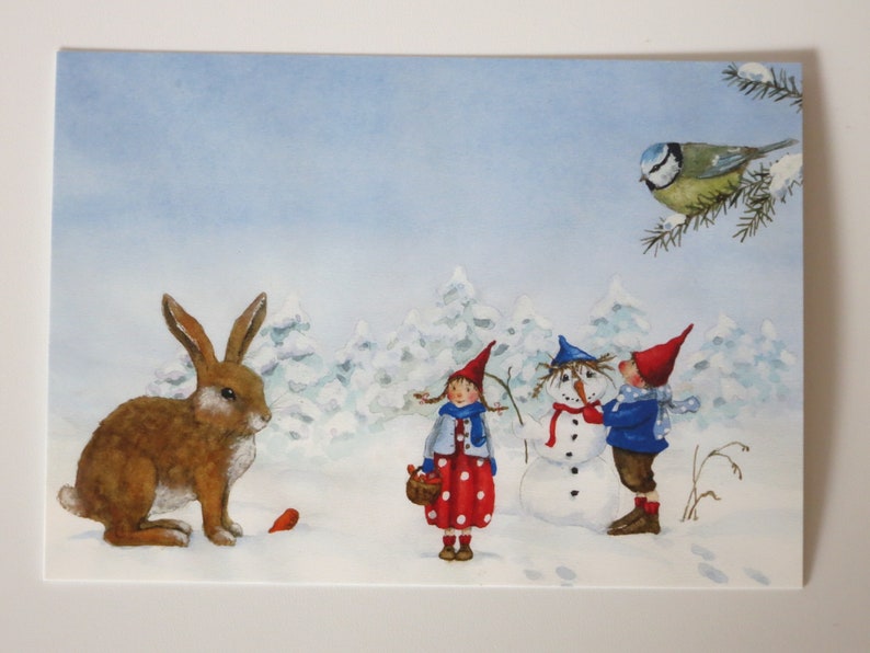May include: A watercolor painting of a winter scene with two children building a snowman. A brown rabbit sits in the snow, and a bluebird perches on a branch in the background.