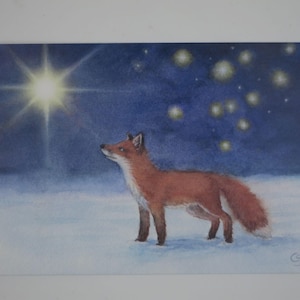 Könnte beinhalten: Aquarellmalerei eines Fuchses, der im Schnee steht und zu einem hellen Stern und anderen leuchtenden Himmelskörpern vor einem dunkelblauen Himmel aufblickt. Der Fuchs hat rotbraunes Fell und einen flauschigen Schwanz.