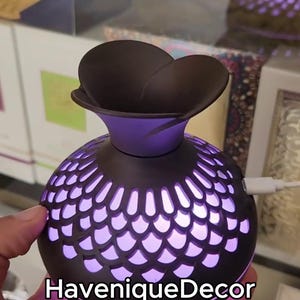 Può includere: Un diffusore per aromaterapia decorativo con una parte superiore floreale marrone scuro e un collo viola. Il corpo sferico è marrone scuro con un motivo a scaglie che si illumina di luce viola. Il testo "HaveniqueDecor" è in basso.