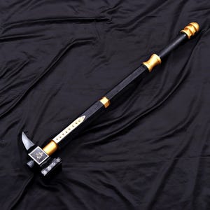 May include: A long-handled war hammer featuring a black shaft with gold-coloured accents and a pommel. The hammer head is black with a silver-coloured spike, a square face displaying a lion emblem, and a side panel decorated with five white crosses.