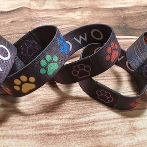 May include: Four black wristbands with paw print designs. One wristband has the word "OWO" printed in white.