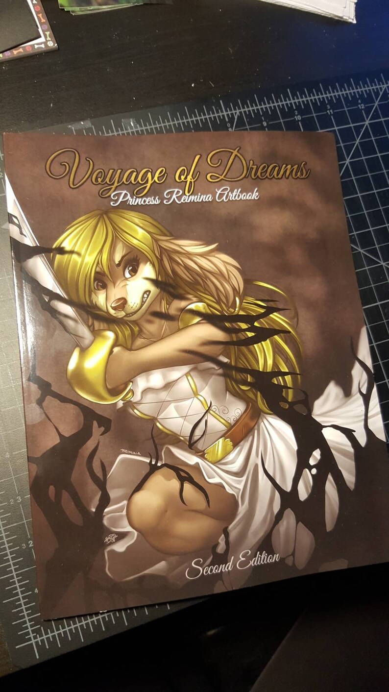May include: A book cover featuring the title "Voyage of Dreams" and "Princess Romina Artbook". The artwork depicts a blonde anthropomorphic character in a white dress, holding a sword, with black shadowy elements. The words "Second Edition" are also visible.