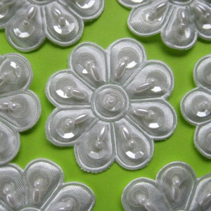 May include: Ten white fabric flower embellishments with pearl-like accents. Each flower has ten petals and a center circle.