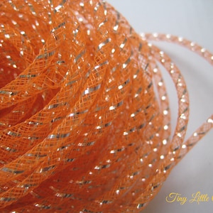 May include: A close-up of a spool of orange and silver metallic mesh ribbon. The ribbon is tightly wound and has a shiny, iridescent finish.