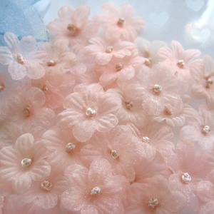 May include: A collection of delicate, pale pink, sheer fabric flowers with a sparkly finish. The flowers have a pearl-like center and are perfect for adding a touch of elegance to crafts and decorations.
