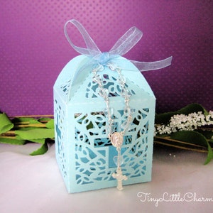 May include: A light blue, laser-cut favor box with a white satin ribbon and a silver rosary inside. The box has a delicate floral design and is perfect for a baptism or communion.
