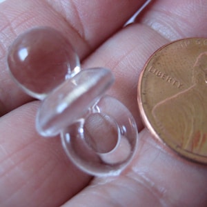 May include: A clear plastic baby pacifier charm, approximately the size of a US penny.