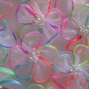 May include: A collection of white tulle bows with multi-colored trim. The bows have a single iridescent bead in the center.
