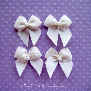 May include: Four white satin bows with pearl centers on a purple polka dot background.