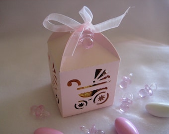 May include: Pink favor box with a cut-out design of a baby carriage. The box is tied with a pink ribbon and has a small pink pacifier attached to the ribbon.