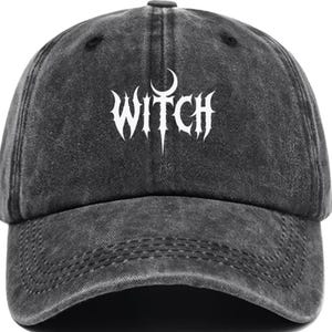 May include: A charcoal grey baseball cap with a distressed, washed-out finish. The front panel features the word WITCH printed in a sharp, white, stylised gothic font, with a crescent moon symbol positioned directly above the letter I.