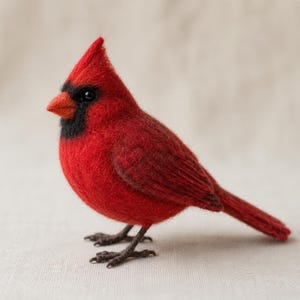 May include: A needle-felted cardinal bird figurine featuring vibrant red wool fibres, a distinct black mask around the eyes, a pointed crest on the head, a small orange beak, and dark brown textured feet, standing in a profile position.