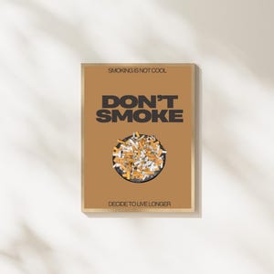 Könnte beinhalten: Ein gerahmtes Poster mit braunem Hintergrund und den Worten "DON'T SMOKE" in fetten schwarzen Buchstaben. Unter dem Text befindet sich ein kreisförmiges Bild von Zigarettenkippen. Oben auf dem Poster steht "SMOKING IS NOT COOL" und unten steht "DECIDE TO LIVE LONGER."