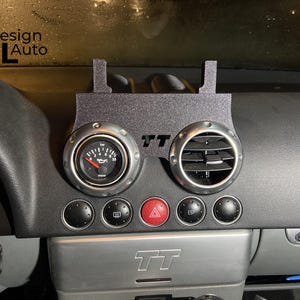 May include: Black dashboard with a custom gauge and vent setup. The gauge reads in bar and has a red needle. The vent is circular with silver trim. The text "TT" is visible. The text "Design MTL Auto" is in the upper left corner.