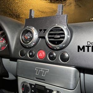 May include: Black dashboard with gauges, air vents, and buttons. A black mounting bracket is attached to the dashboard. The dashboard has the text "Design MTL Auto".
