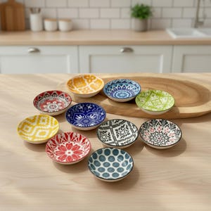 May include: A collection of small, decorative ceramic bowls with colorful, intricate patterns. The bowls feature various designs in shades of red, yellow, blue, and green, perfect for serving dips or snacks. The bowls are arranged on a wooden surface.