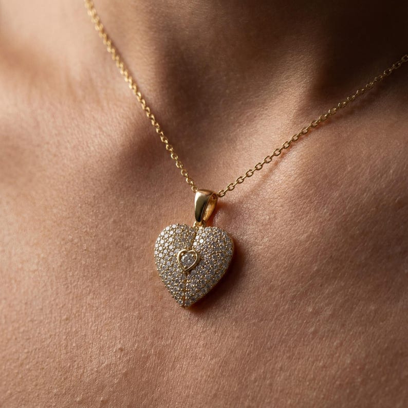 Close-up of a dainty pavé heart pendant necklace on a delicate gold chain. The 925 sterling silver heart is covered in small sparkling stones with a tiny raised heart detail and fine center line, shown on a woman’s neck and in hand, minimalist jewelry style, ideal Valentines gift for her.