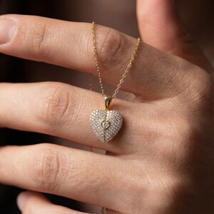 Puede incluir: Un collar dorado con un colgante en forma de coraz&oacute;n. El colgante est&aacute; incrustado con peque&ntilde;as piedras preciosas transparentes y presenta un coraz&oacute;n m&aacute;s peque&ntilde;o en el centro. El collar tiene una cadena fina.