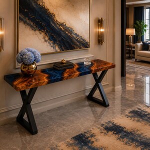 Puede incluir: Una mesa consola rectangular con un tablero de madera de borde natural y una incrustación central de resina azul, sostenida por dos patas de metal negro en forma de X. Un jarrón dorado con hortensias azules se sitúa sobre la mesa.