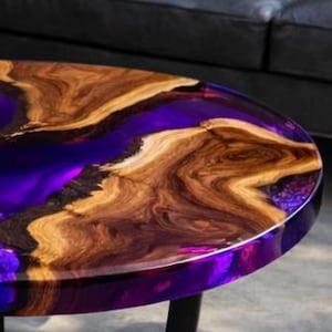 May include: Round coffee table with a wood and resin design. The table features a dark purple resin center and a natural wood grain border. The table is approximately 30 inches in diameter.