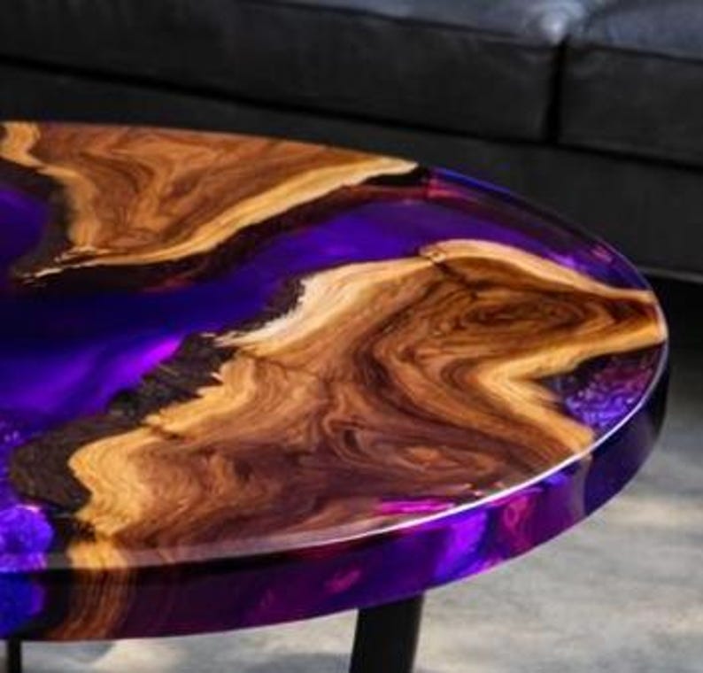 May include: Round coffee table with a wood and resin design. The table features a dark purple resin center and a natural wood grain border. The table is approximately 30 inches in diameter.