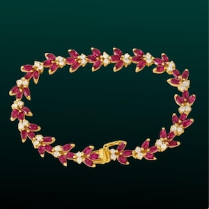 Könnte beinhalten: Ein goldenes Armband mit floralem Design, das rubinrote Edelsteine und kleine Cluster weißer Edelsteine aufweist. Das Armband hat einen sicheren Verschluss und ist vor einem dunkelgrünen Hintergrund platziert.