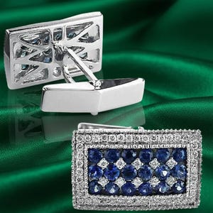 May include: A pair of rectangular cufflinks featuring a silver-toned metal frame. The face of each cufflink is set with a grid of round, deep blue stones interspersed with smaller, clear white stones, surrounded by a border of tiny clear crystals.