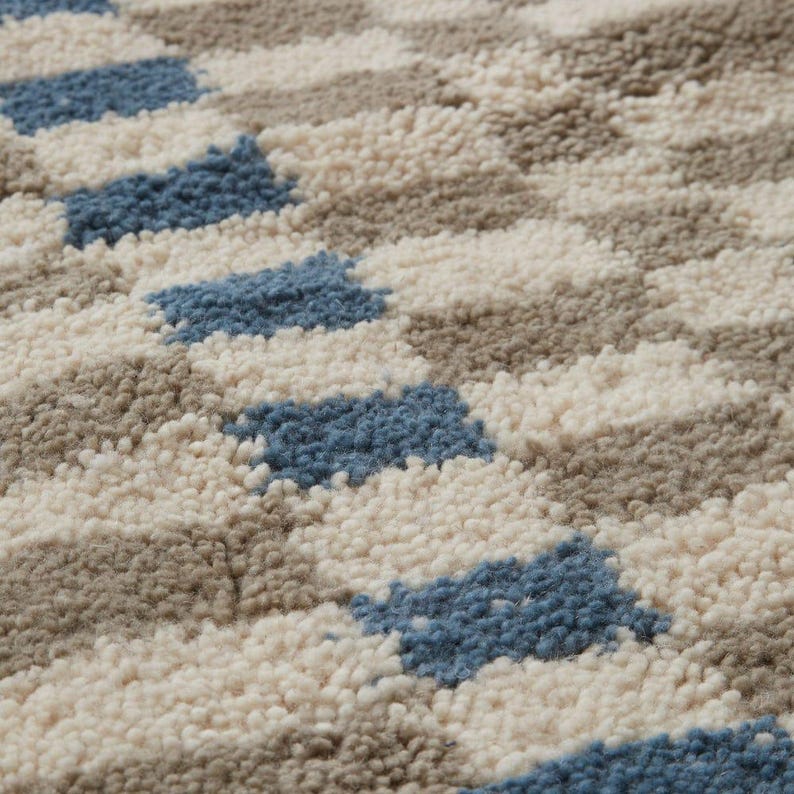 K&ouml;nnte beinhalten: Nahaufnahme eines strukturierten Teppichs mit geometrischem Muster. Der Teppich weist ein sich wiederholendes Design aus blauen, beigen und grauen Formen auf. Die weiche Textur und die neutrale Farbpalette schaffen eine gem&uuml;tliche und einladende &Auml;sthetik.