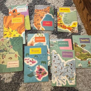 May include: A collection of vintage travel guidebooks featuring colorful illustrations of various destinations. The books showcase maps and cultural depictions of places like Greece, Portugal, and Mexico. The covers have a retro design.