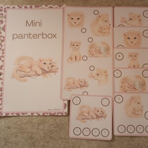 May include: A set of pink and white cards and a notebook with a leopard print border. The cards feature illustrations of lion cubs and adult lions. The notebook reads "Mini panterbox" in brown text. The cards have numbered circles.