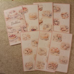 Könnte beinhalten: Eine Sammlung rosa-weißer Rezeptkarten mit Aquarellillustrationen von Backwaren und Backutensilien. Die Karten zeigen Kuchen, Kekse und das Wort "Bakken".