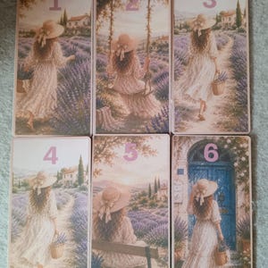 May include: Six rectangular bookmarks featuring illustrations of a person in a white dress and straw hat in a lavender field. Each bookmark is numbered one through six, depicting scenes with a house, a swing, a path, and a blue door.
