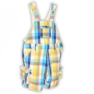 May include: Short overalls in a plaid pattern of yellow, blue, and white. The garment has adjustable straps, pockets on the front and sides, and button closures. The overall is designed for a child.