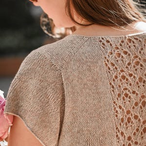 Puede incluir: Top de punto beige con un diseño de espalda calada único. La parte superior de manga corta tiene un escote redondo y un patrón de punto texturizado. La espalda presenta un intrincado patrón similar al encaje, agregando un toque delicado a la prenda.