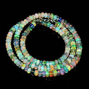 May include: A necklace composed of numerous small, faceted, round opal beads. Each bead displays a translucent base with iridescent flashes of green, blue, orange, and pink. The strand is secured with a silver-toned metal clasp at the top.