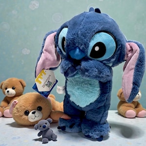May include: A plush blue Stitch doll with large eyes, ears, and a tag. Several brown teddy bears and a small gray bear are also visible. The Stitch doll is the focal point, with a soft, textured appearance.