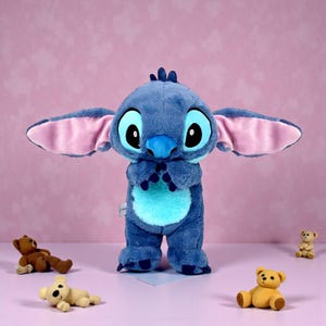 May include: A large blue plush toy of the character Stitch from the Disney movie Lilo & Stitch, with large ears and big eyes. Several small teddy bear toys are scattered around the plush toy on a pink background.