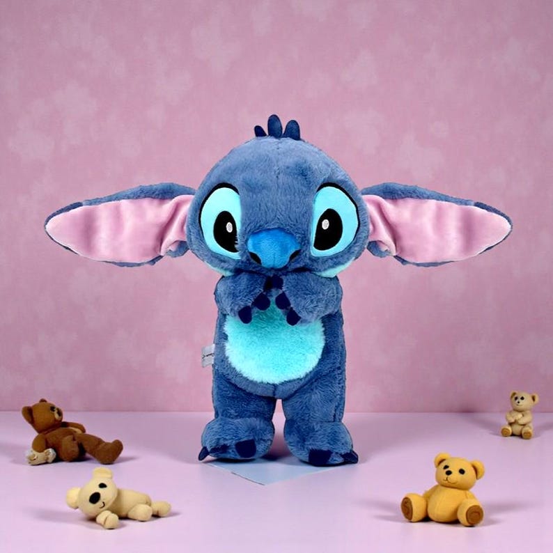 May include: A large blue plush toy of the character Stitch from the Disney movie Lilo & Stitch, with large ears and big eyes. Several small teddy bear toys are scattered around the plush toy on a pink background.