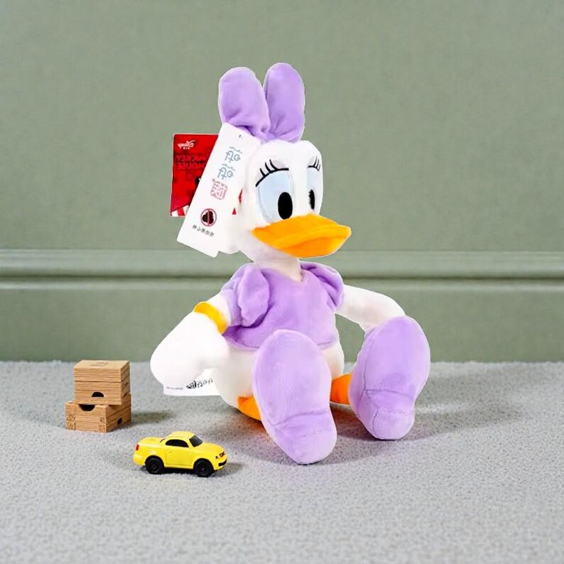 May include: A Daisy Duck plush toy with a purple dress, ears, and feet, and a white body. A small yellow toy car and wooden blocks are in front of the plush toy. A tag is attached to the plush toy.