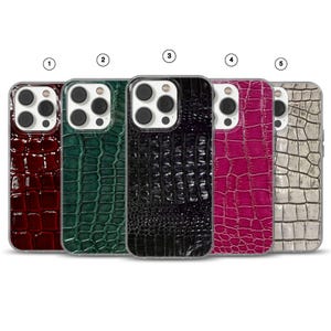 Op de afbeelding: Vijf telefoonhoesjes met een krokodillenleertextuur. De hoesjes zijn verkrijgbaar in de kleuren bordeauxrood, donkergroen, zwart, magenta en zilver. Elke hoes heeft een transparante rand rond de camera en de telefoonranden.