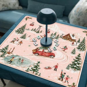 May include: A dark blue mushroom-shaped lamp sits on a square mat featuring a pink winter landscape illustration with a red car, pine trees, a frozen pond, and people skiing. Several white mahjong tiles are scattered around the lamp base.